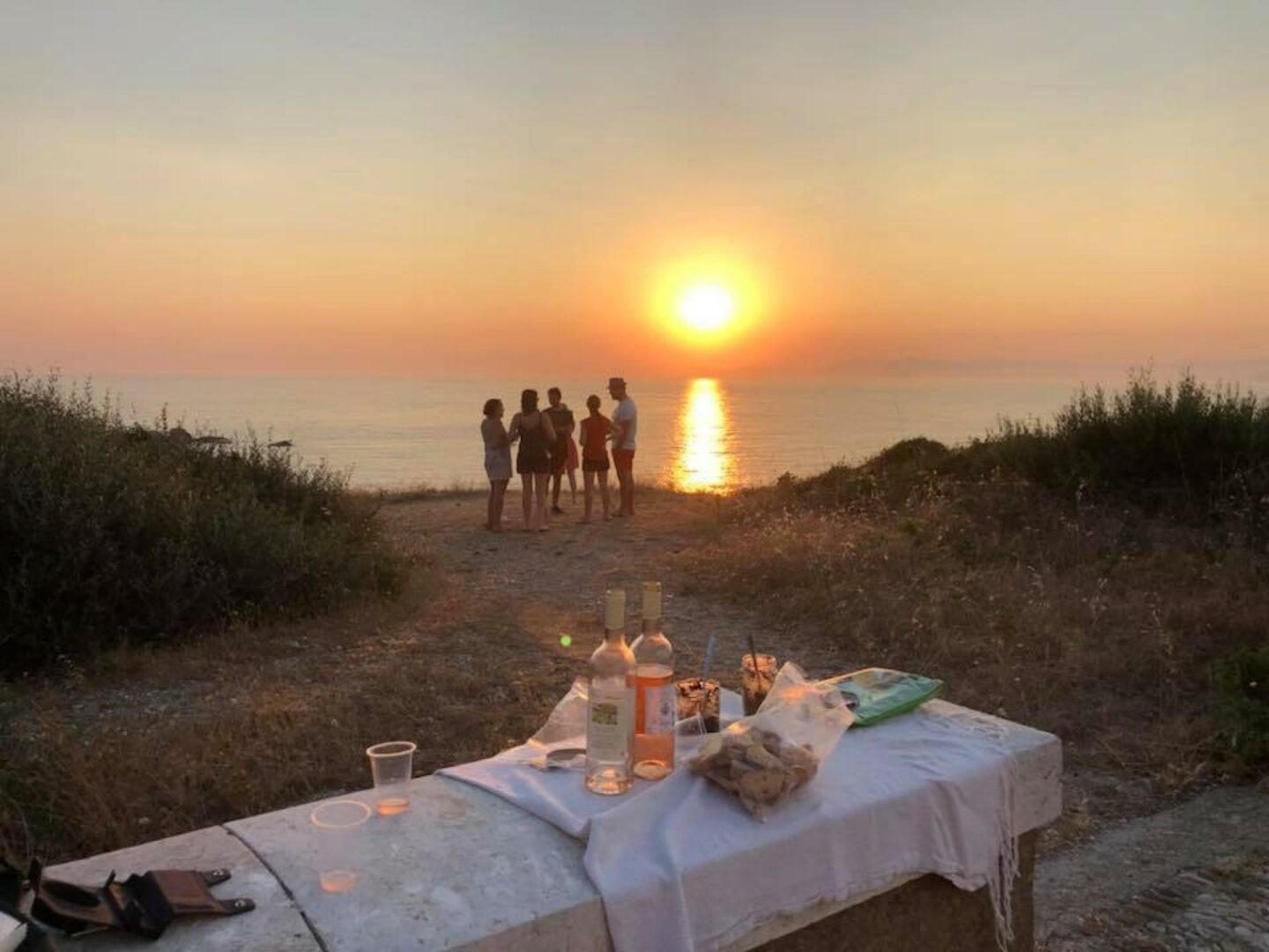 Friends sharing a sunset picnic with rosé wine by the Mediterranean Sea in Provence